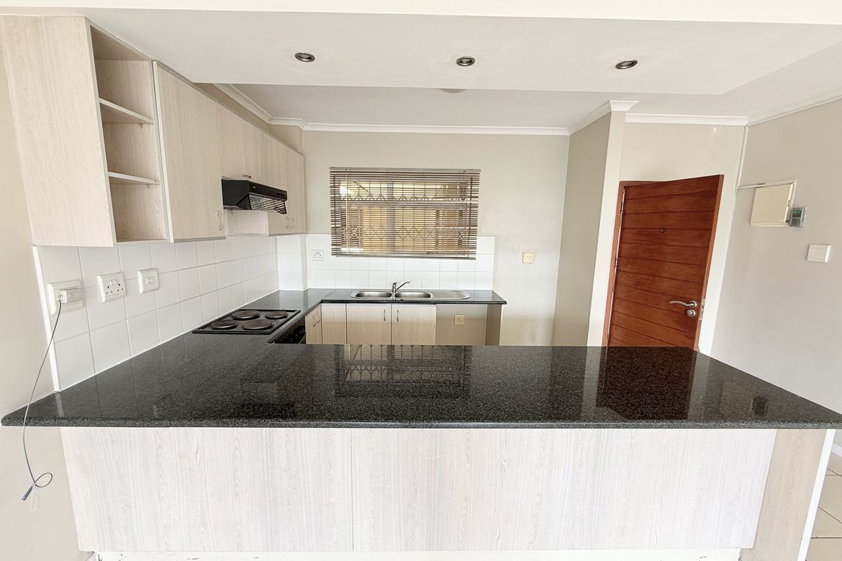 A functional kitchen featuring granite countertops, built-in cabinetry, an electric hob with extractor, and a double basin sink with tiled backsplash.
