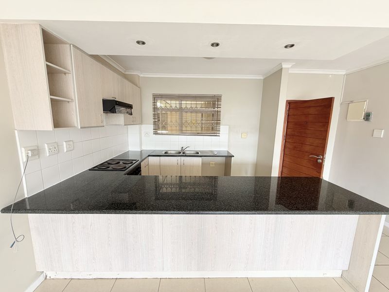 A functional kitchen featuring granite countertops, built-in cabinetry, an electric hob with extractor, and a double basin sink with tiled backsplash.