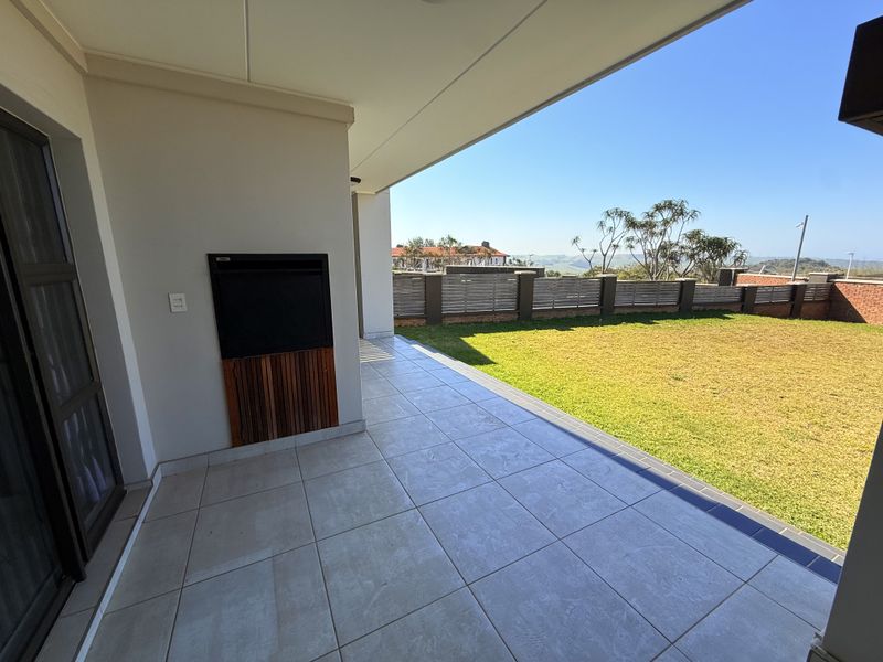 A spacious covered patio featuring a built-in braai, tiled flooring, and direct access to a private garden area with scenic views.