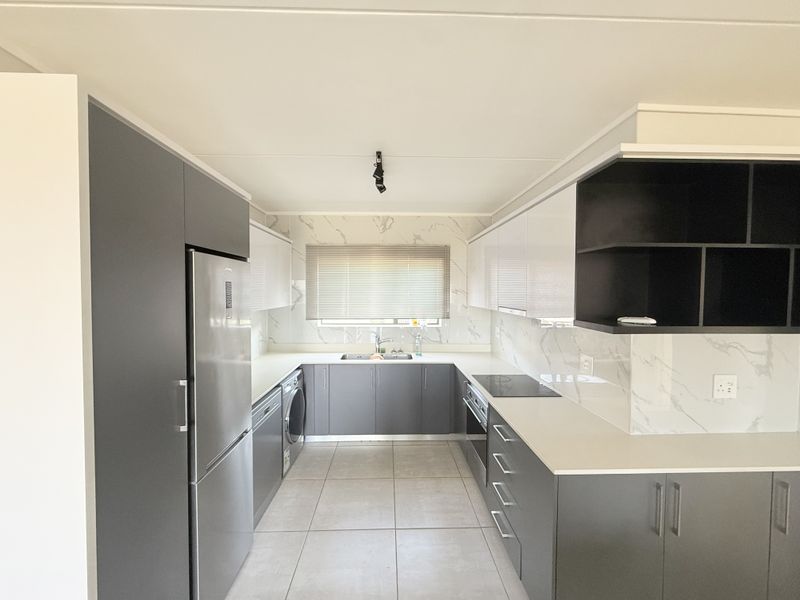 Modern, U-shaped kitchen featuring sleek grey and white cabinetry, marble-look splashbacks, stone countertops, and integrated appliances in a clean, contemporary finish.