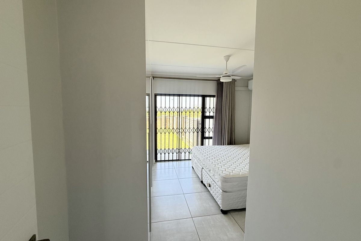 A bright bedroom featuring tiled flooring, a ceiling fan, and a sliding door with a security gate leading to the exterior.
