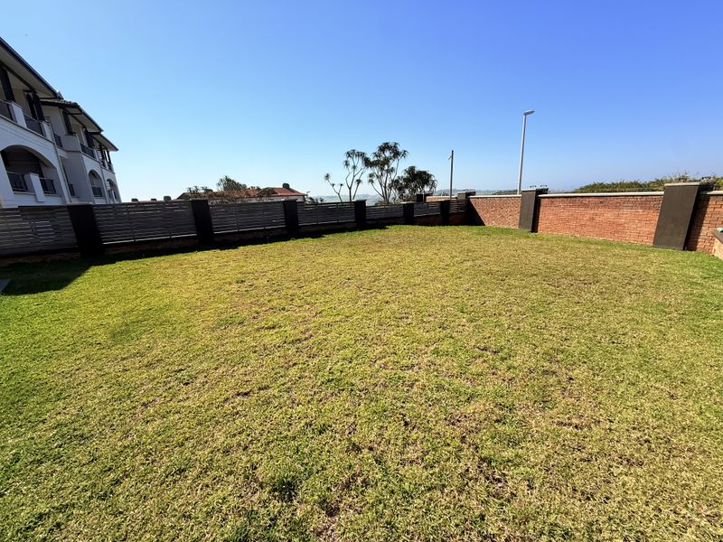 A spacious, well-maintained private garden area featuring a level lawn, enclosed by a combination of brick boundary walls and slatted timber fencing.
