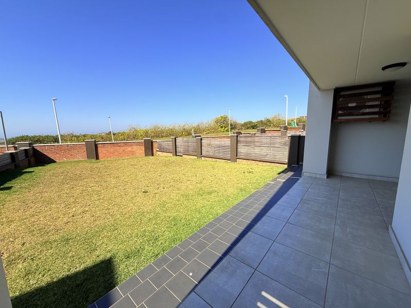 A spacious covered patio featuring tiled flooring, overlooking a private garden area enclosed by brick walls and timber fencing.