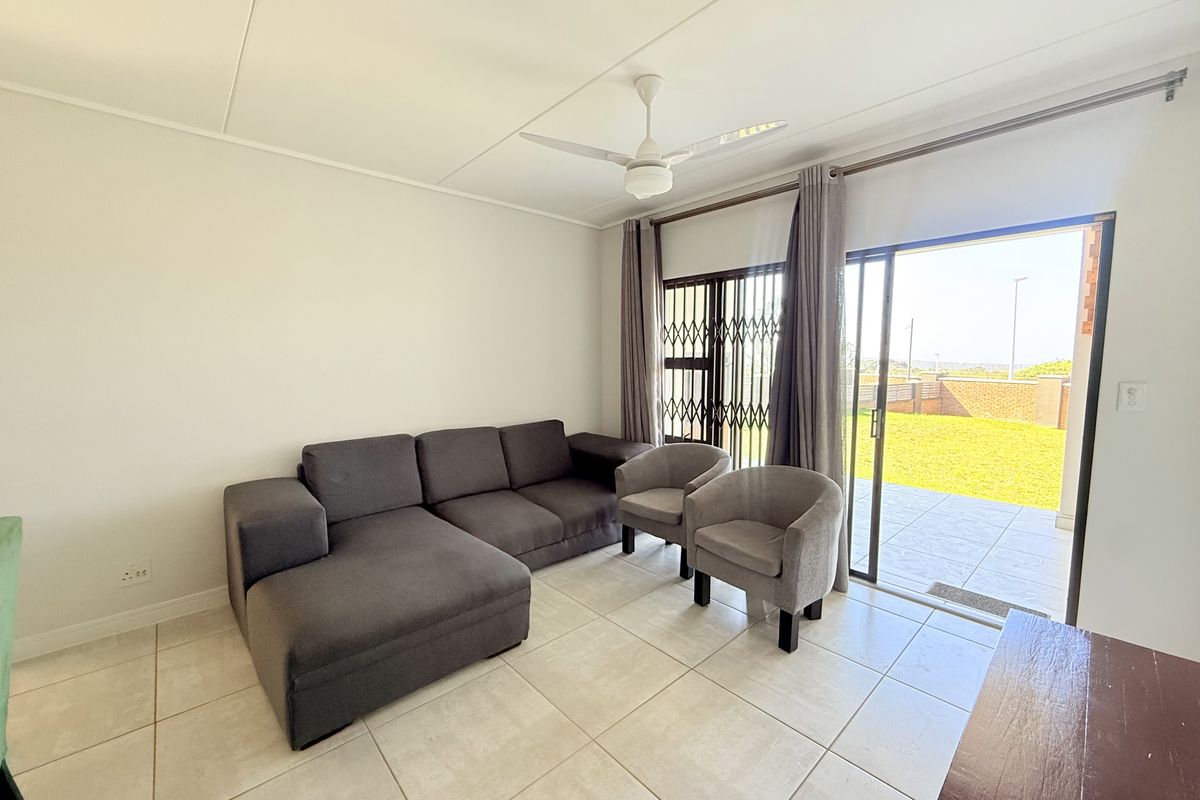 Bright living room featuring neutral tiled flooring, a ceiling fan, and direct access through a sliding glass door to an outdoor tiled patio area.