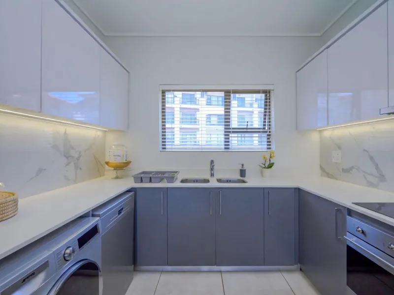 Modern kitchen featuring sleek white and grey cabinetry, marble-look splashbacks, integrated appliances, and under-cabinet lighting, providing a clean and functional workspace.