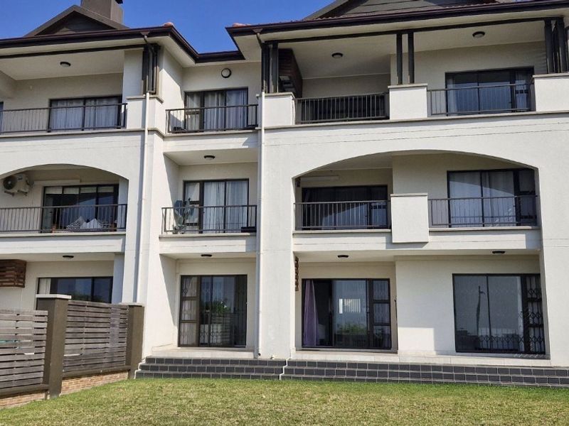 Rear elevation of a multi-story apartment complex featuring private balconies, sliding glass doors, and a landscaped garden area with timber fencing.