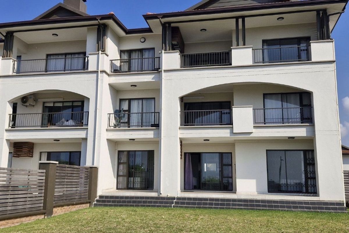 Rear elevation of a multi-story apartment complex featuring private balconies, sliding glass doors, and a landscaped garden area with timber fencing.