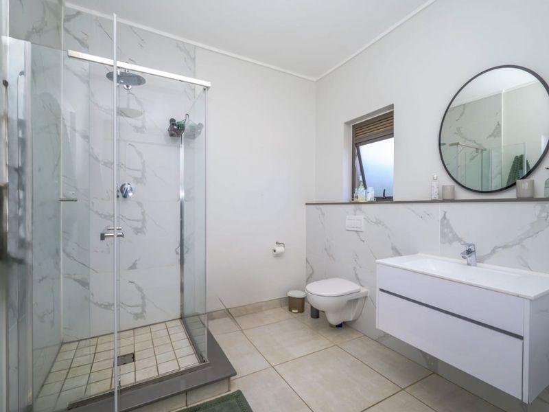 Modern bathroom featuring a glass-enclosed shower, wall-mounted toilet, and a sleek floating vanity with marble-look wall tiling.