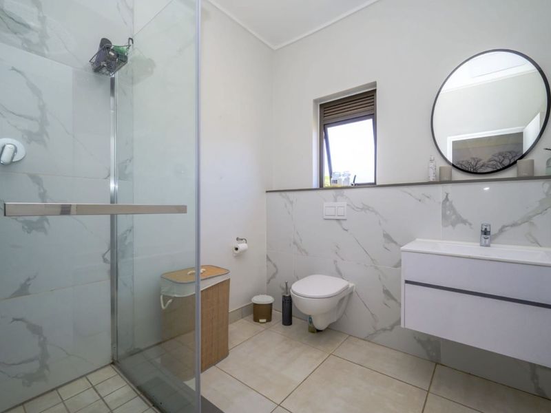 Modern bathroom featuring a walk-in shower with glass screen, wall-mounted toilet, floating vanity, and elegant marble-look wall tiling.