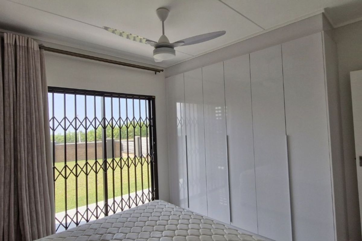 A well-maintained bedroom featuring modern built-in cupboards, a ceiling fan, air conditioning, and a sliding door with security gate access to the outdoors.