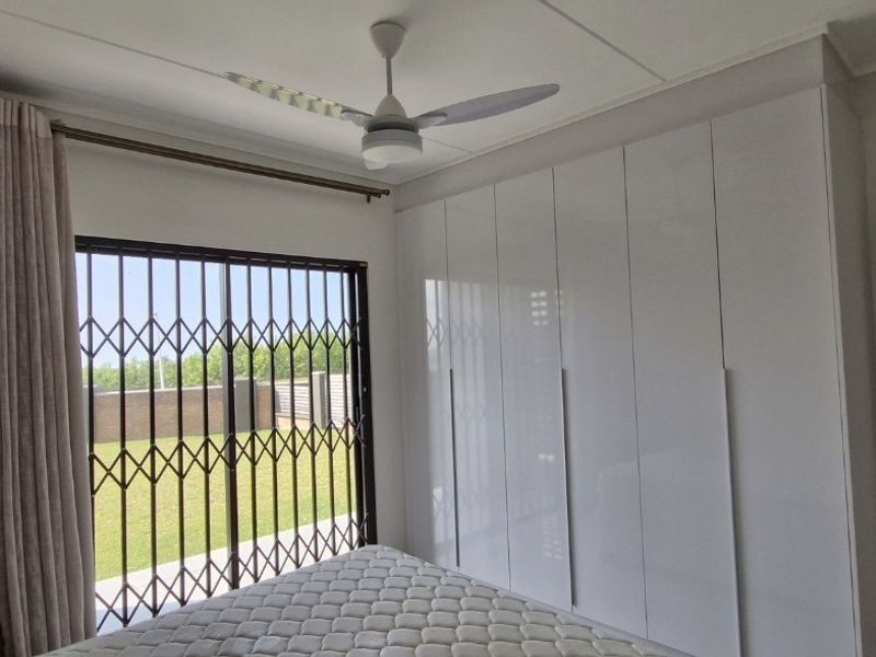 A well-maintained bedroom featuring modern built-in cupboards, a ceiling fan, air conditioning, and a sliding door with security gate access to the outdoors.
