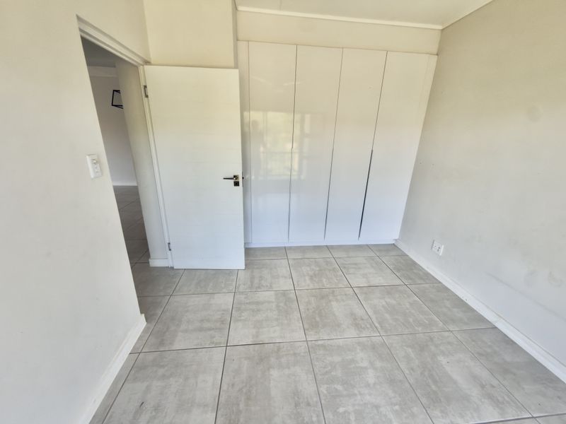 A clean, empty bedroom featuring neutral tiled flooring and modern white built-in cupboards, offering a blank canvas for personalization.