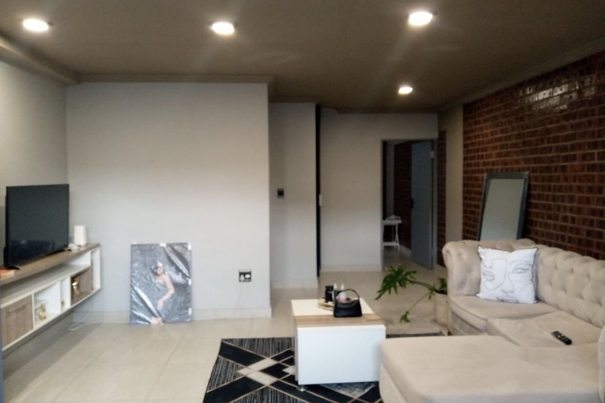 A contemporary living room featuring a striking exposed brick wall, neutral tiled flooring, recessed ceiling lighting, and a sleek floating media console.
