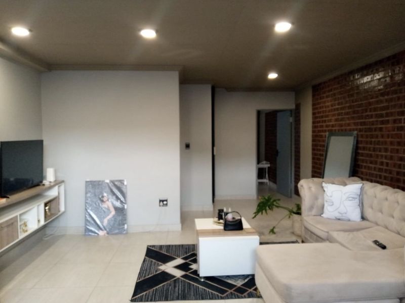 A contemporary living room featuring a striking exposed brick wall, neutral tiled flooring, recessed ceiling lighting, and a sleek floating media console.