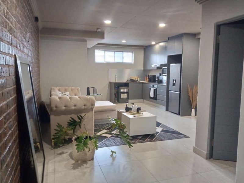 Modern open-plan living area featuring a contemporary kitchen with sleek cabinetry, integrated appliances, and a striking exposed brick feature wall.