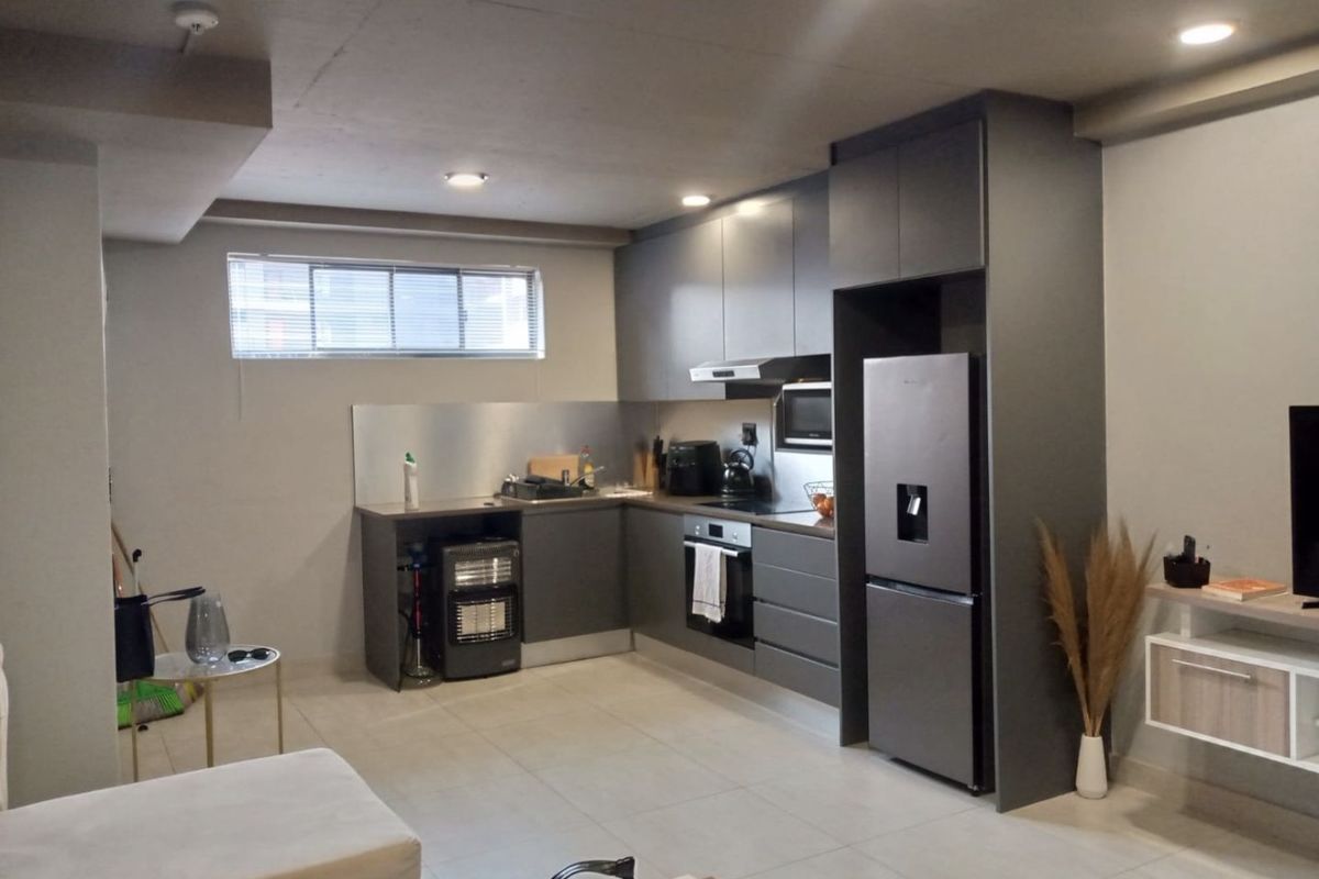 Modern open-plan kitchen featuring dark grey cabinetry, integrated appliances, stainless steel splashback, and recessed lighting, seamlessly flowing into the living area.