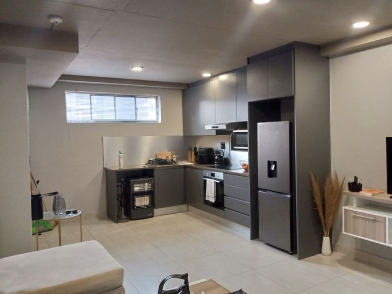 Modern open-plan kitchen featuring dark grey cabinetry, integrated appliances, stainless steel splashback, and recessed lighting, seamlessly flowing into the living area.