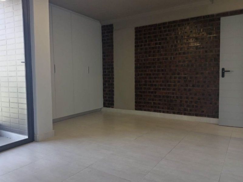 An empty bedroom featuring modern tiled flooring, built-in cupboards, and a stylish exposed brick feature wall with access to an outdoor area.