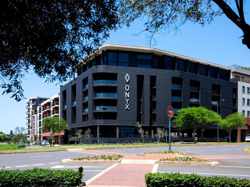 A modern multi-story apartment building featuring a dark facade, glass balconies, and a prominent street-level entrance, situated in a well-maintained urban environment.