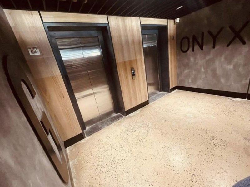 A modern apartment building elevator lobby featuring wood-paneled walls, polished concrete flooring, and dual elevator access.
