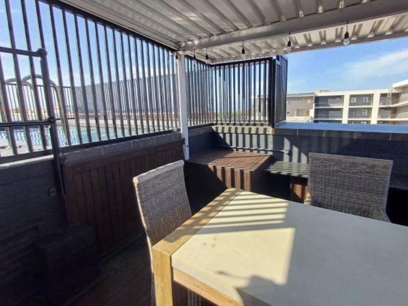 A covered balcony featuring a corrugated metal roof, metal security railings, and built-in wooden cabinetry, providing a functional outdoor entertainment space.