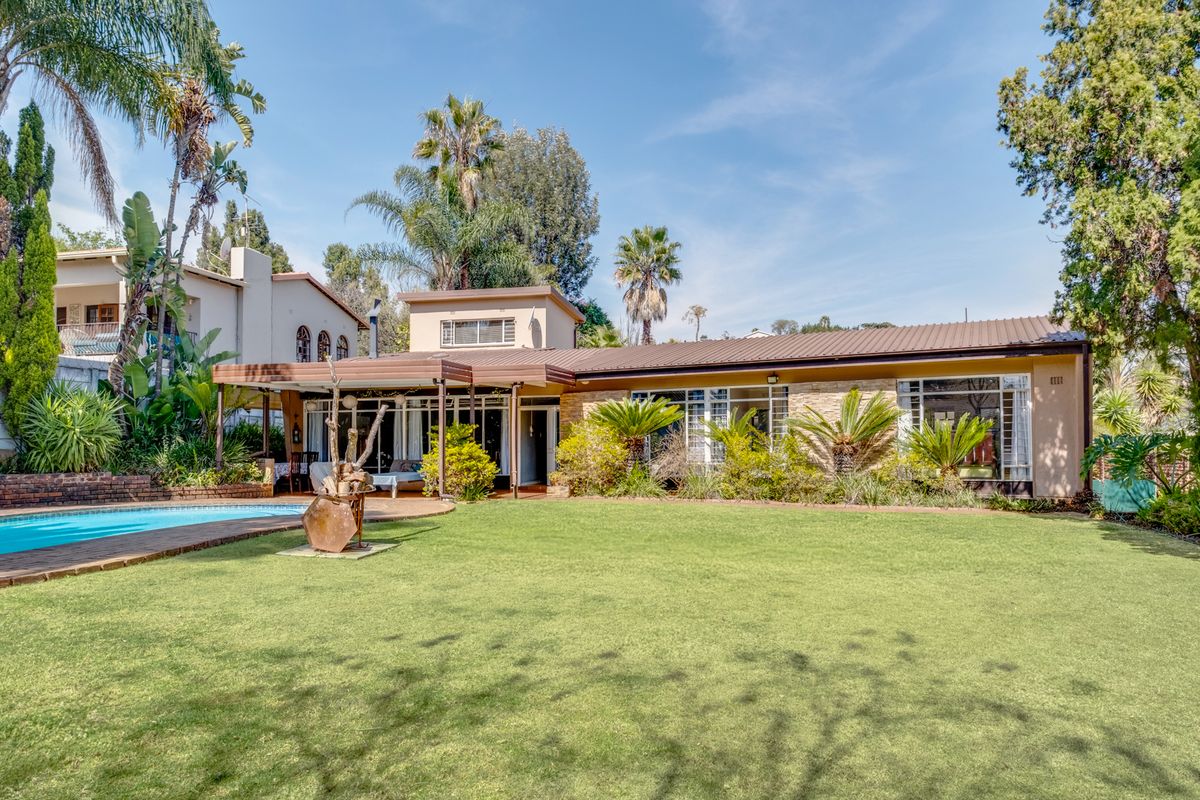 Rear view of the property featuring a well-maintained garden, swimming pool, and a covered patio area with stone cladding accents.