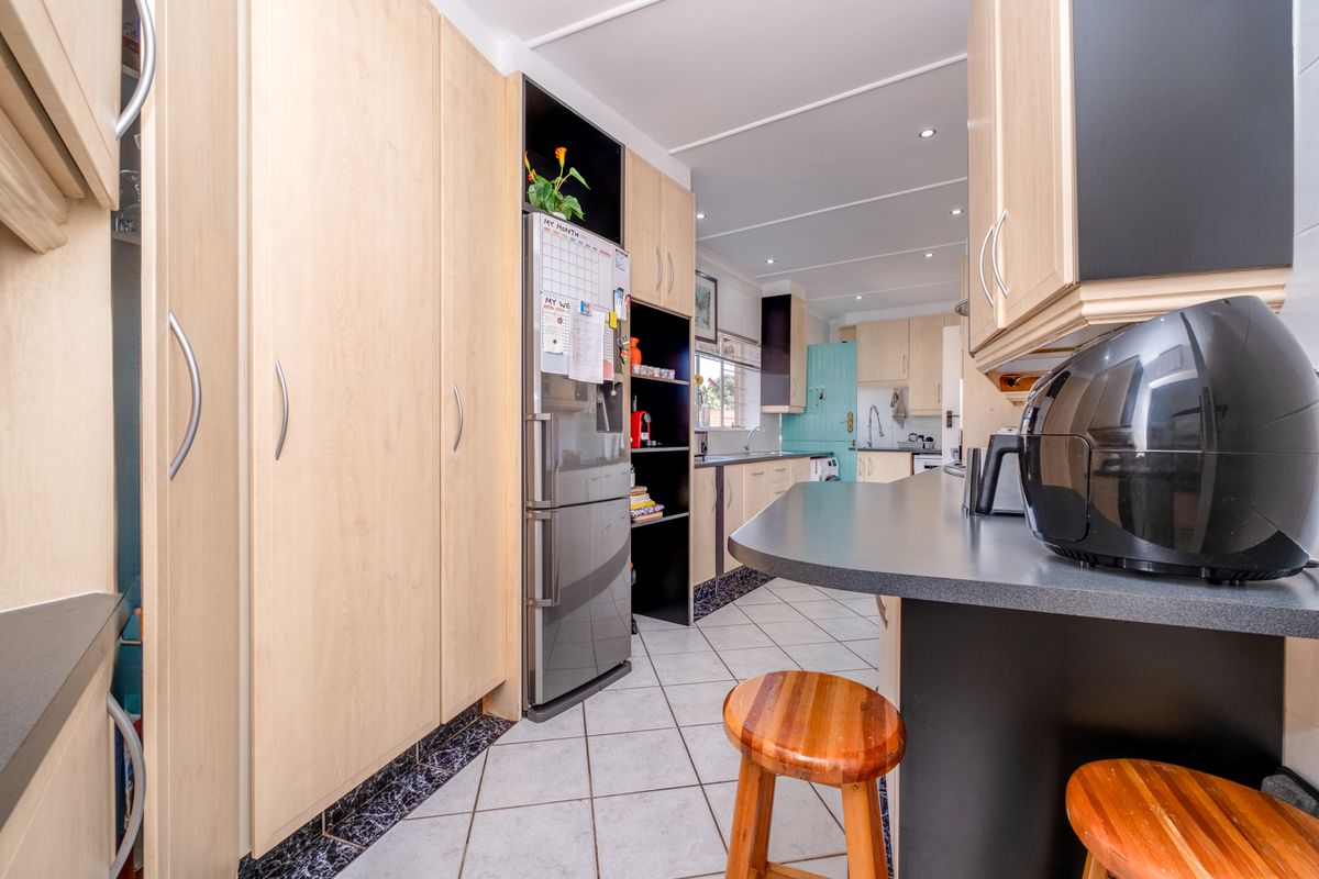 Functional kitchen featuring light wood cabinetry, dark laminate countertops, a breakfast bar, and tiled flooring with a practical layout.
