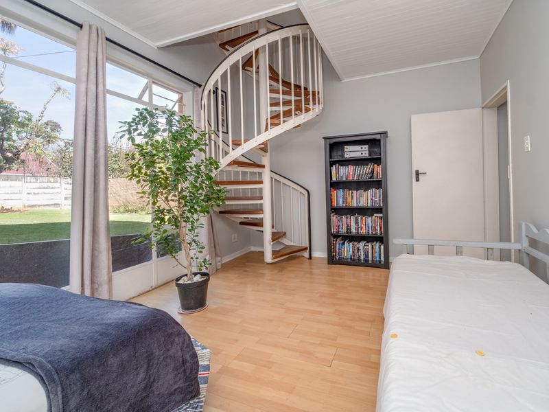 A bright bedroom featuring a distinctive spiral staircase, laminate flooring, and large glass doors providing natural light and garden views.