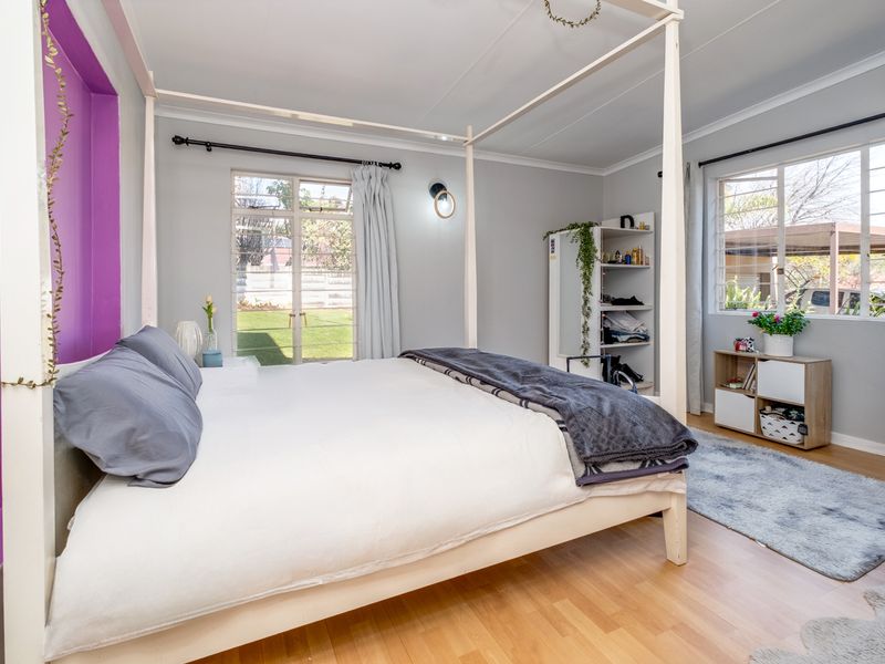 A bedroom featuring laminate flooring, a recessed purple accent wall, and large windows providing natural light and garden views.