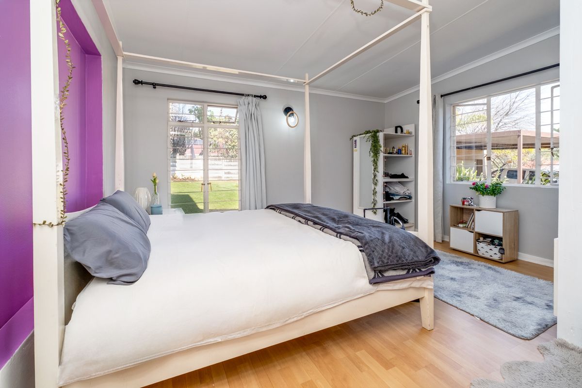A bedroom featuring laminate flooring, a recessed purple accent wall, and large windows providing natural light and garden views.