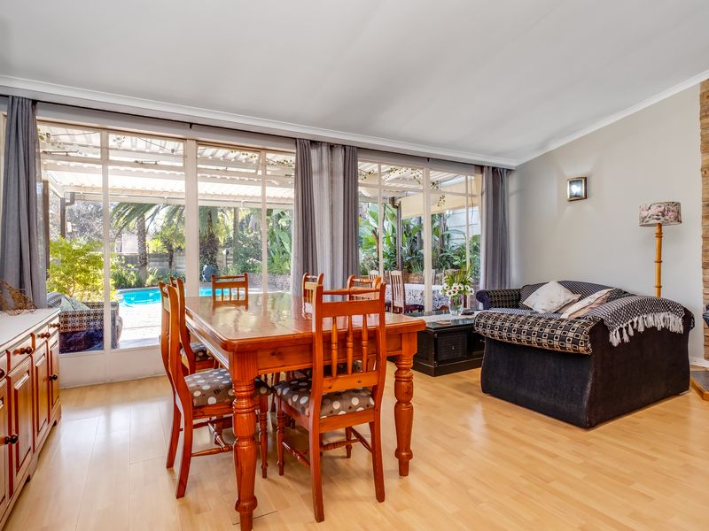 Open plan living and dining area featuring laminate flooring, a stone feature wall, and large sliding glass doors providing access to the patio and pool.