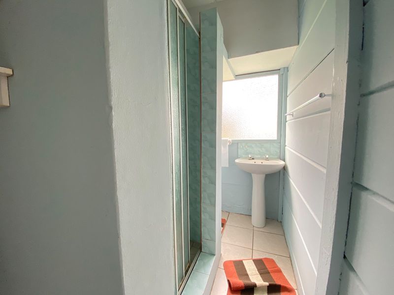 A compact bathroom featuring a pedestal sink, a shower enclosure with tiled surround, and tiled flooring, requiring cosmetic updates.