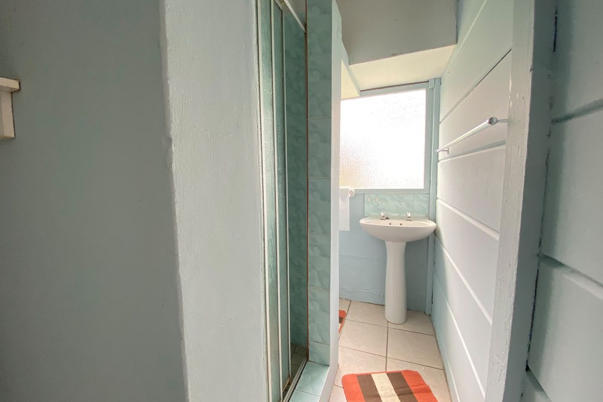 A compact bathroom featuring a pedestal sink, a shower enclosure with tiled surround, and tiled flooring, requiring cosmetic updates.