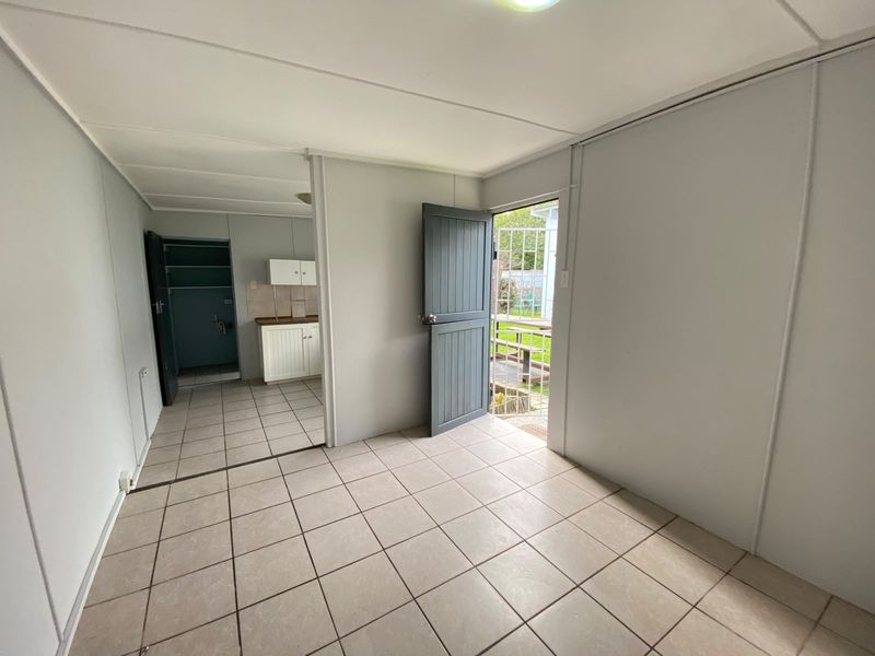 An open-plan living area with tiled flooring, leading to a small kitchen space and an exterior door with a security gate.