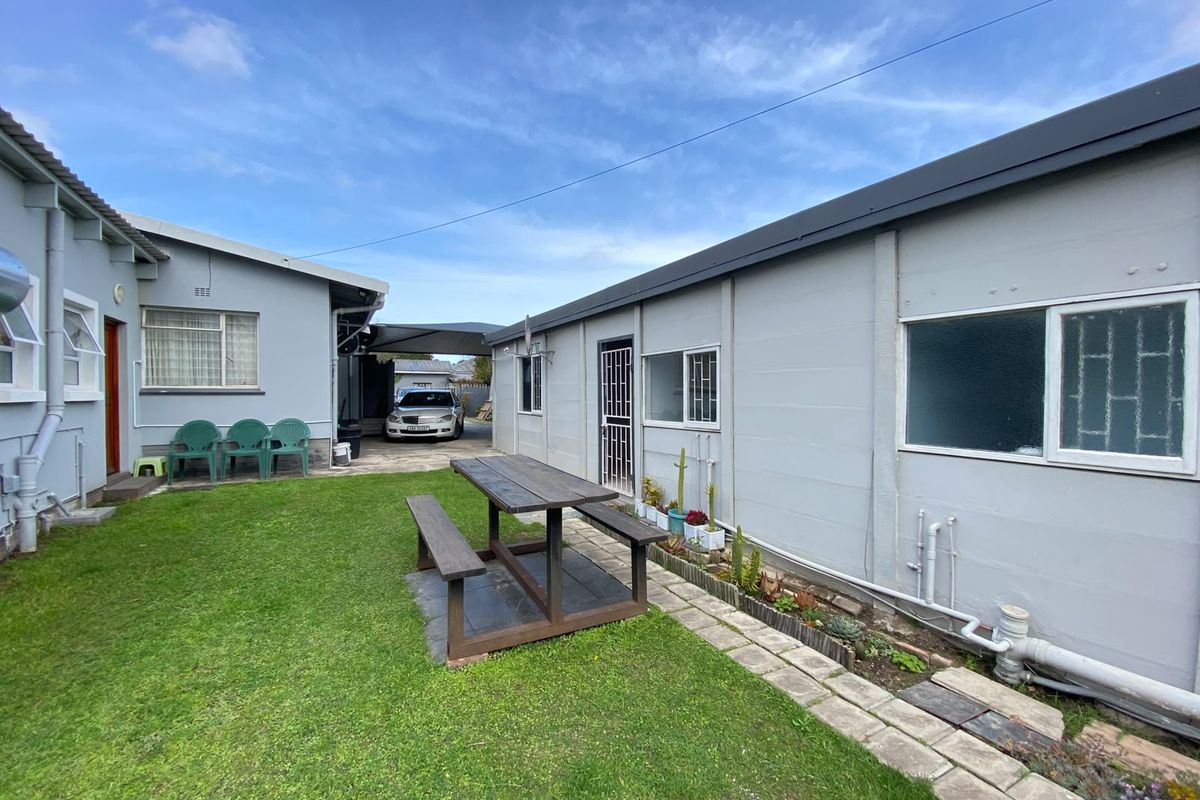A rear courtyard area featuring a lawn, paved walkway, and exterior building access with security gates and bars on windows.