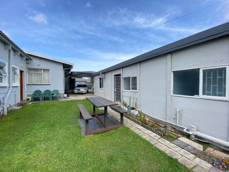 A rear courtyard area featuring a lawn, paved walkway, and exterior building access with security gates and bars on windows.