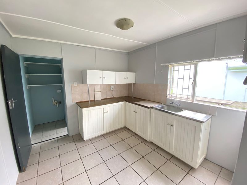 A functional kitchen featuring white cabinetry, tiled flooring, a stainless steel sink, and an adjacent pantry area with built-in shelving.