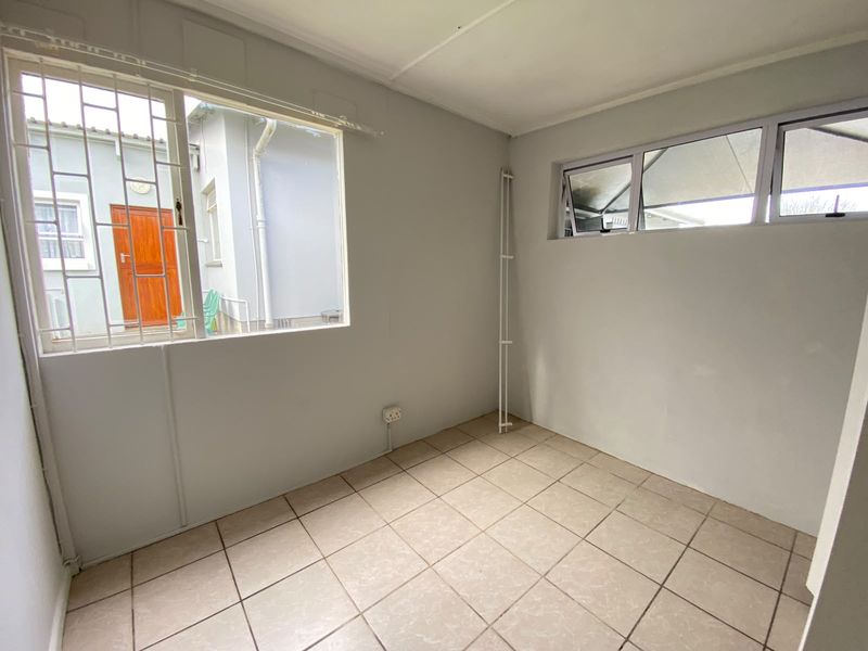 A clean, empty bedroom featuring neutral tiled flooring, security bars on the windows, and ample natural light.