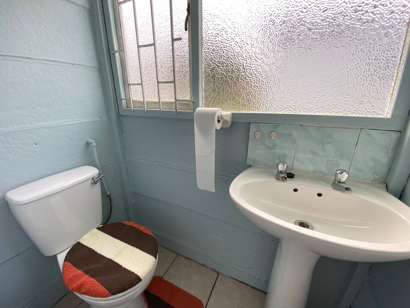 A compact bathroom featuring a pedestal basin, toilet, and security-barred window with obscured glass, requiring cosmetic updates to modernize the space.