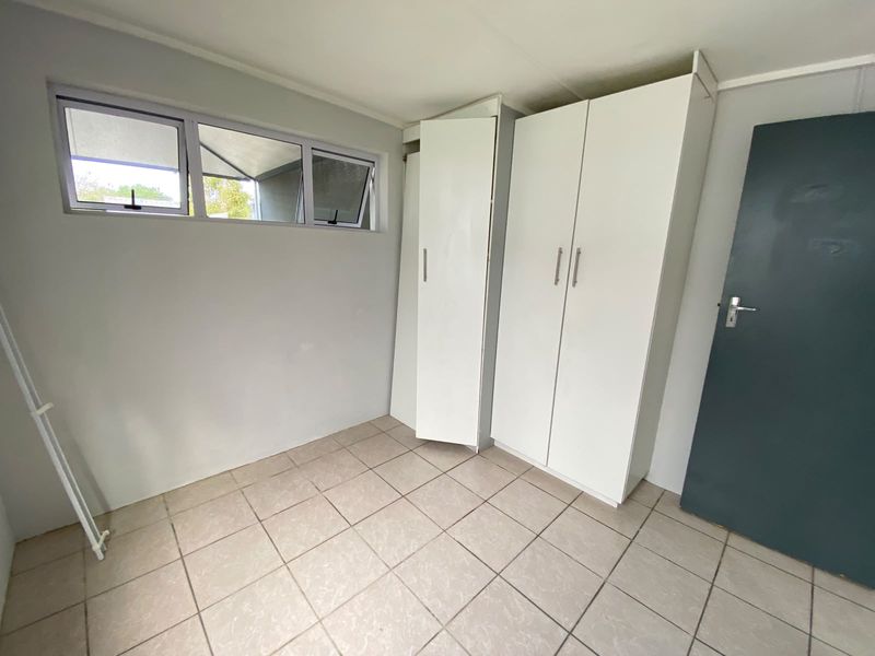 A clean, empty bedroom featuring neutral tiled flooring, built-in white cupboards, and top-hung windows providing natural light.