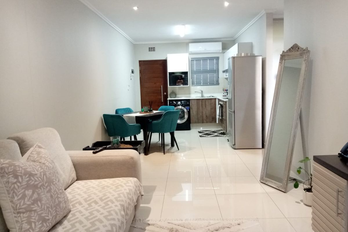 Modern open-plan living area featuring tiled floors, recessed lighting, and a compact kitchen with built-in cabinetry and integrated appliances.