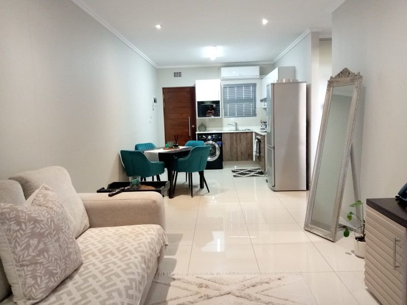 Modern open-plan living area featuring tiled floors, recessed lighting, and a compact kitchen with built-in cabinetry and integrated appliances.