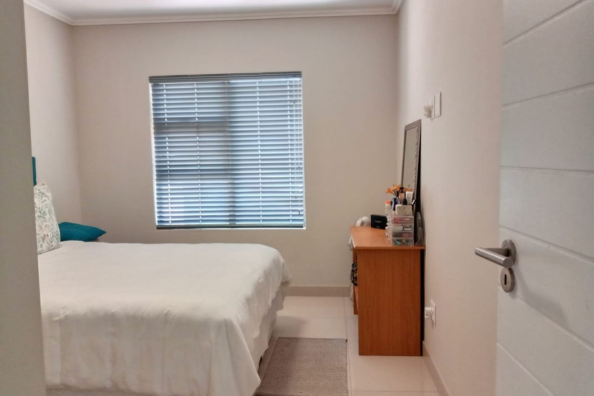 A well-maintained bedroom featuring neutral tiled flooring, a window with fitted venetian blinds, and a standard internal door.