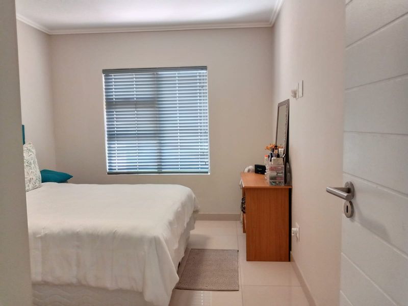 A well-maintained bedroom featuring neutral tiled flooring, a window with fitted venetian blinds, and a standard internal door.