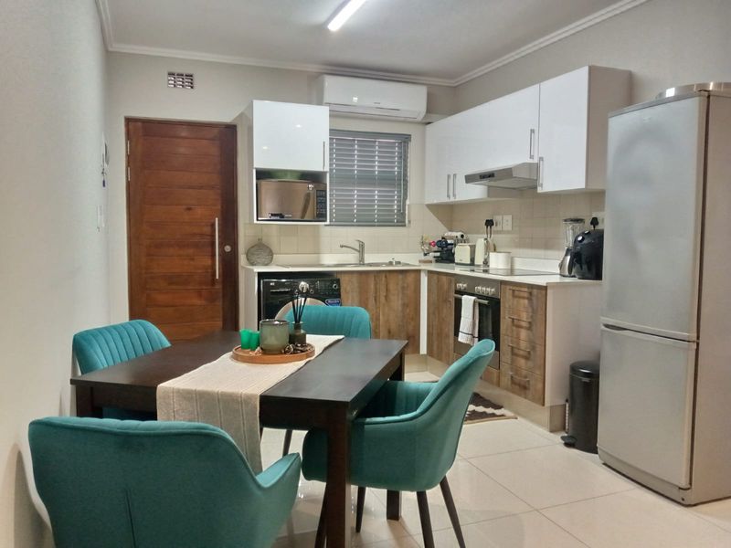 Modern open-plan kitchen and dining area featuring sleek cabinetry, built-in appliances, tiled flooring, and an integrated air conditioning unit.