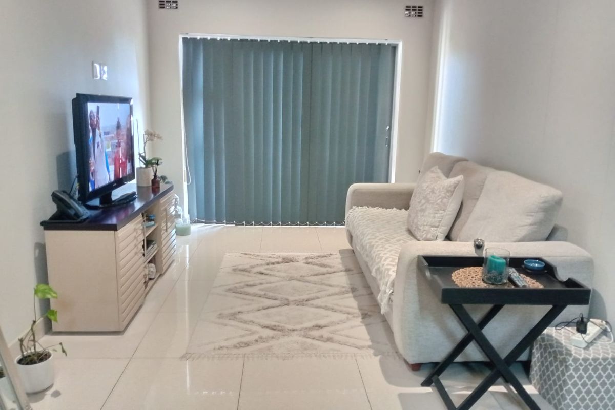 A well-maintained living room featuring neutral tiled flooring, recessed ceiling ventilation, and a large sliding glass door fitted with vertical blinds.