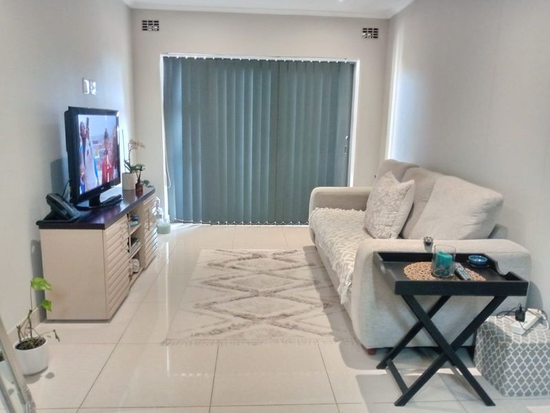 A well-maintained living room featuring neutral tiled flooring, recessed ceiling ventilation, and a large sliding glass door fitted with vertical blinds.