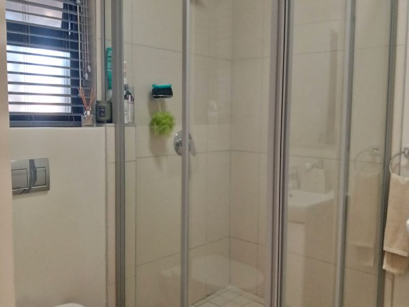 A functional bathroom featuring a corner shower enclosure with glass doors, a wall-mounted toilet, and neutral wall tiling.