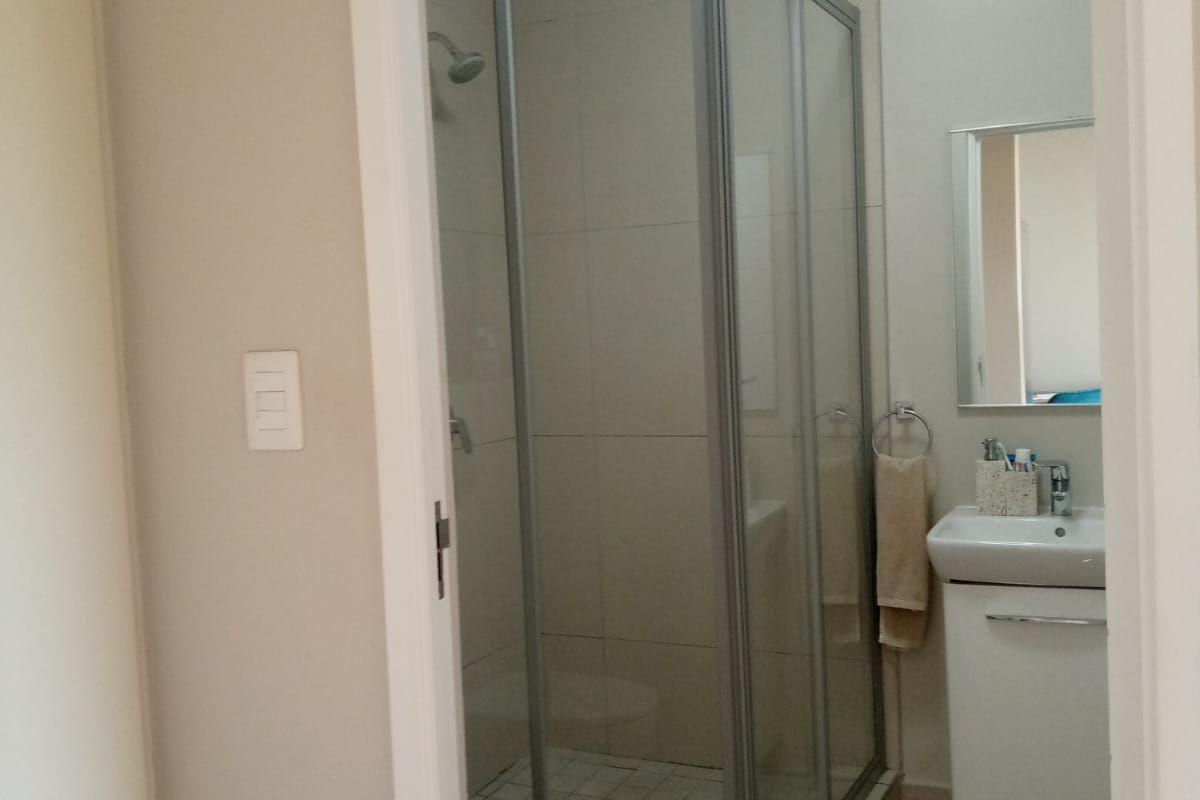 A functional bathroom featuring a corner shower enclosure, a wall-mounted vanity with a basin, and neutral wall and floor tiling.