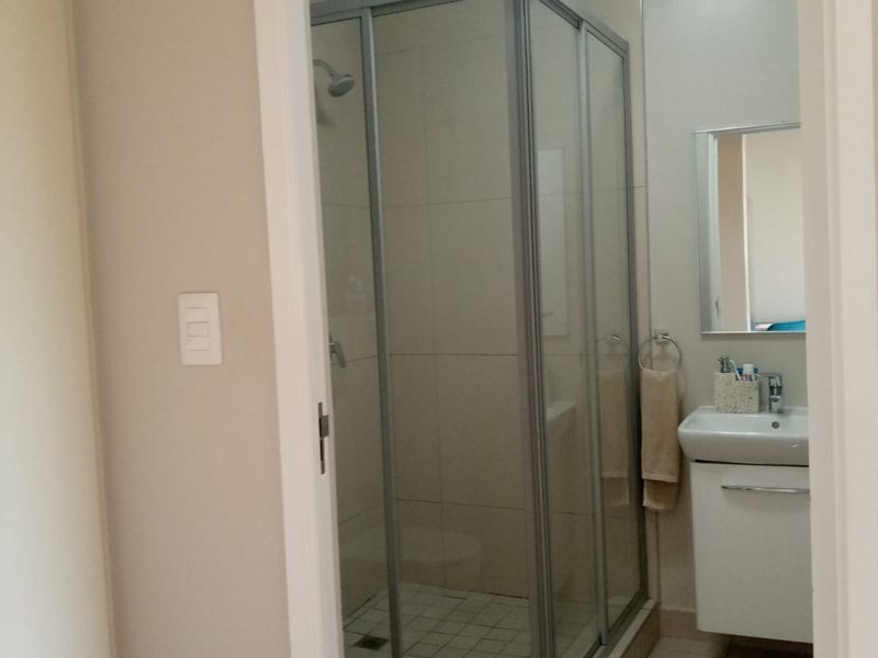 A functional bathroom featuring a corner shower enclosure, a wall-mounted vanity with a basin, and neutral wall and floor tiling.
